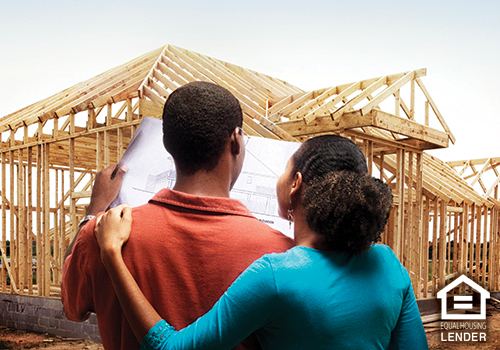 Couple looking at blueprints in front of house under construction
